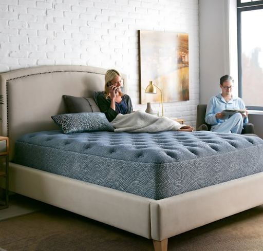 lady-sitting-on-bed-with-husband-working-nearby